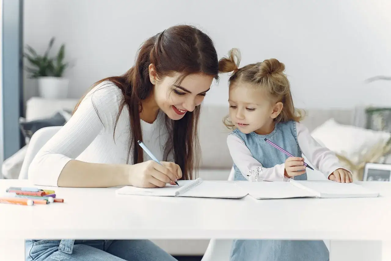 Mama z córką piszą w zeszytach. To przykład wydłużenia etapu edukacyjnego, gdzie nauka trwa dłużej.