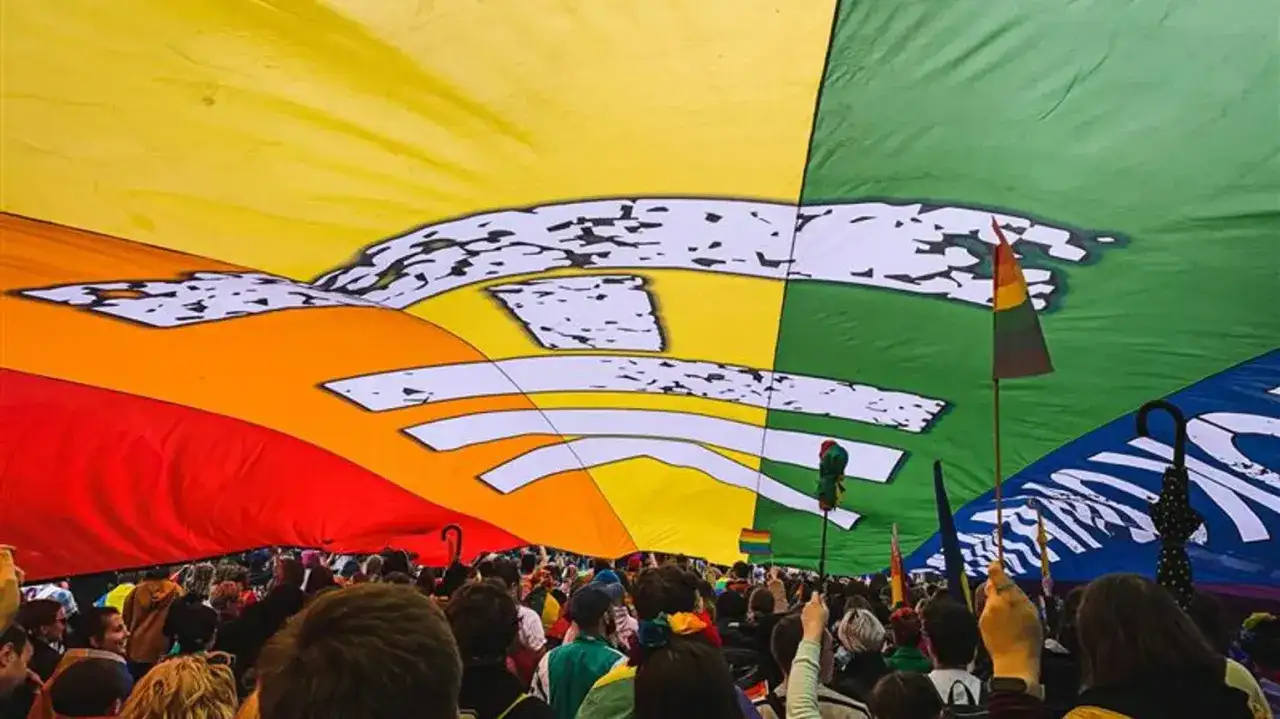 Tęczowa flaga symbolizuje wsparcie dla lgbt w szkołach. Tłum ludzi pod gigantyczną flagą.
