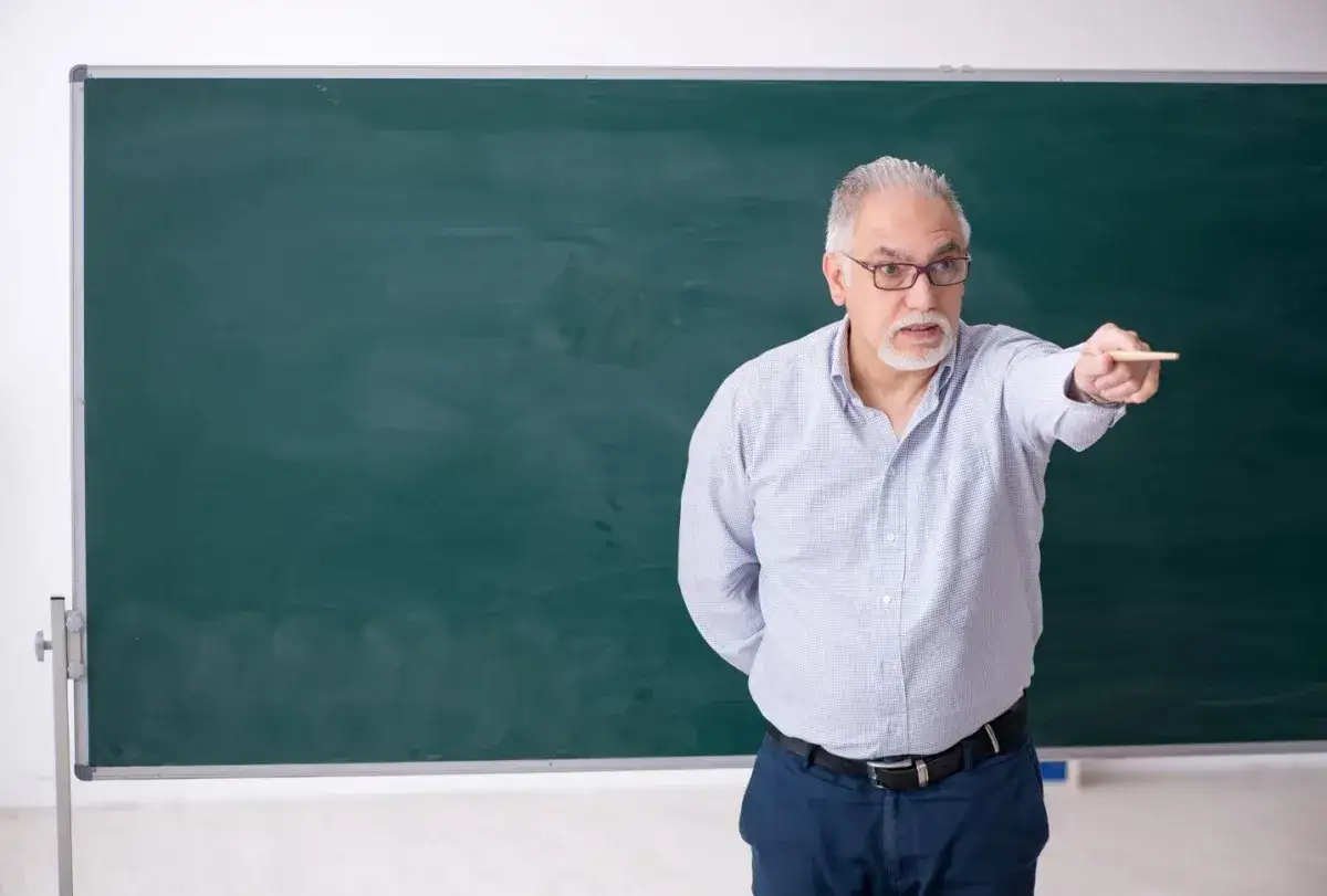 Nauczyciel z kredą przy tablicy, gotowy do rozpoczęcia lekcji. To świadczenie na start dla nauczycieli, wspierające ich w edukacji.
