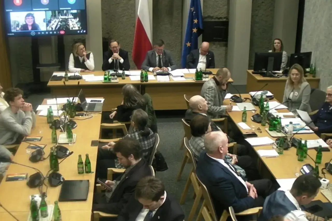 Dyskusja o edukacji seksualnej w szkołach. Ludzie siedzą przy stołach, niektórzy patrzą na ekran, inni notują.