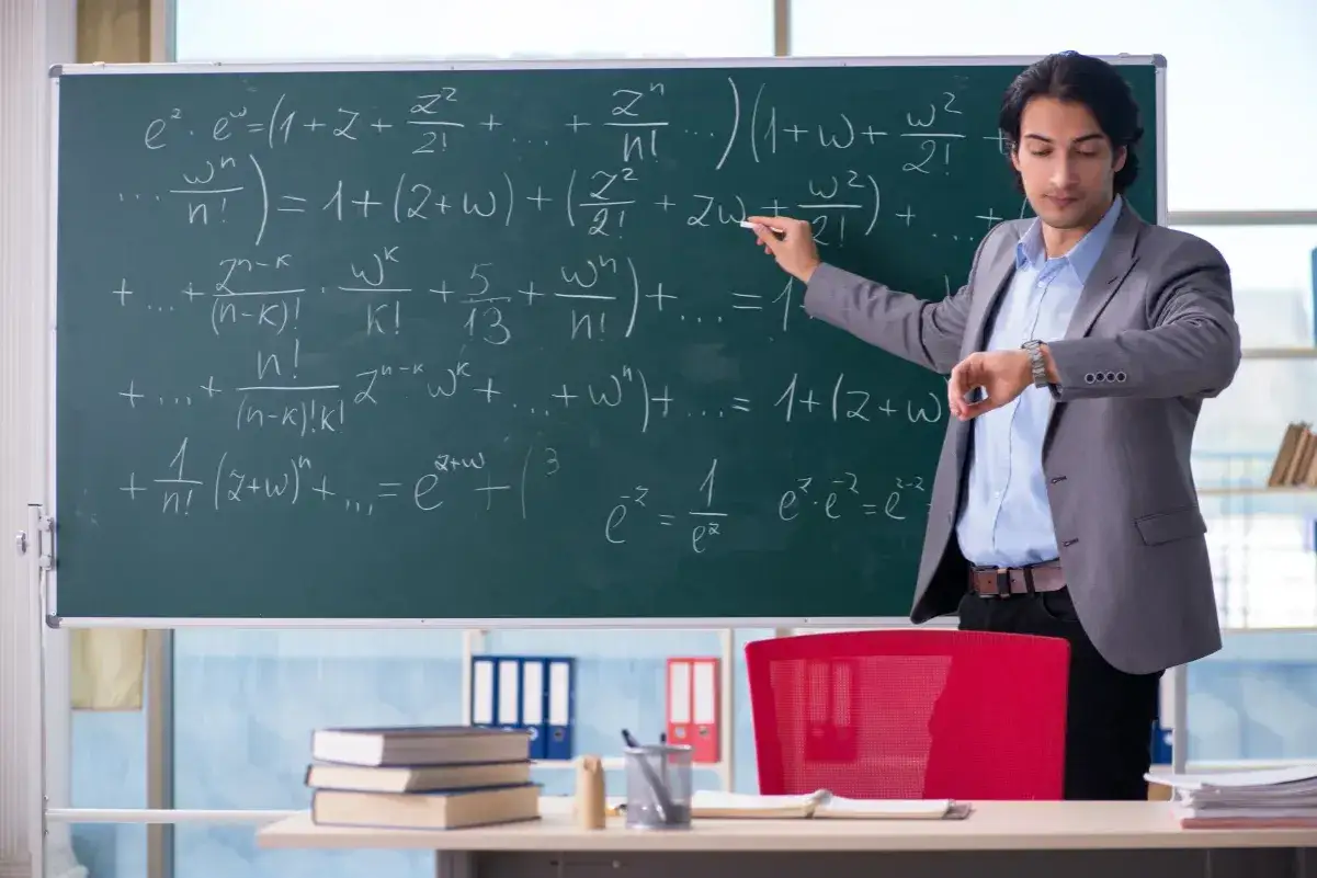 Nauczyciel matematyki pisze wzory na tablicy, sprawdzając zegarek. To świadczenie na start dla nauczycieli, którzy chcą rozwijać swoje umiejętności.