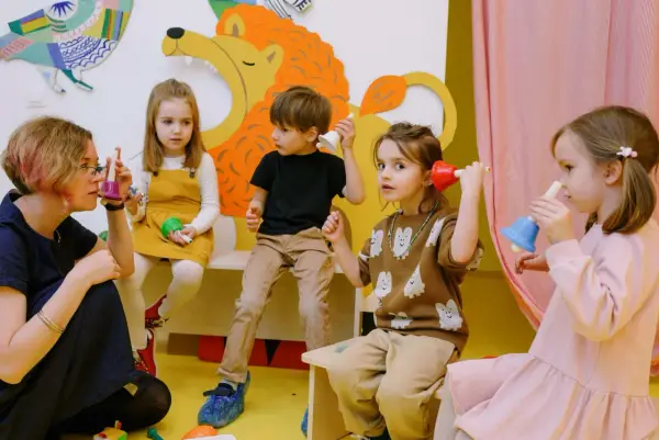 Nauczycielka i dzieci bawią się dzwonkami. Kto może prowadzić tus? Dzieci na zajęciach muzycznych.